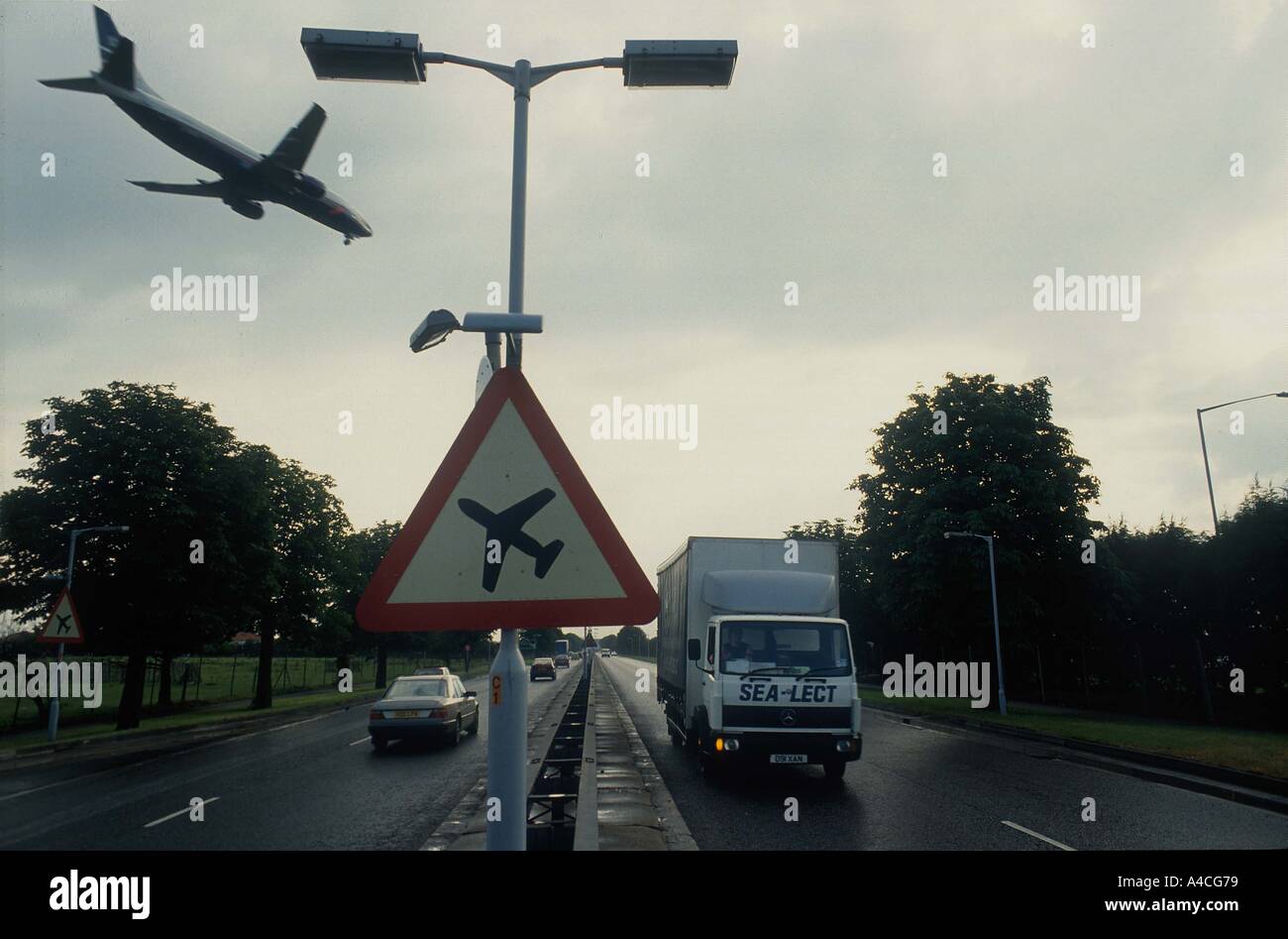 Aeromobile proveniente per atterrare all'aeroporto di Londra Heathrow vola su una strada principale molto trafficata passato un segno di avvertimento di bassa aeromobile in volo Foto Stock