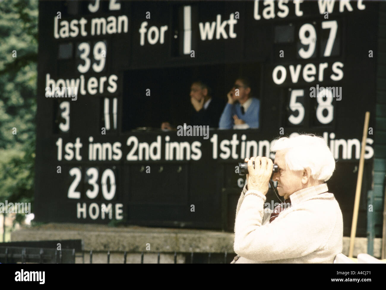 Uomo anziano guarda il cricket attraverso il binocolo Foto Stock
