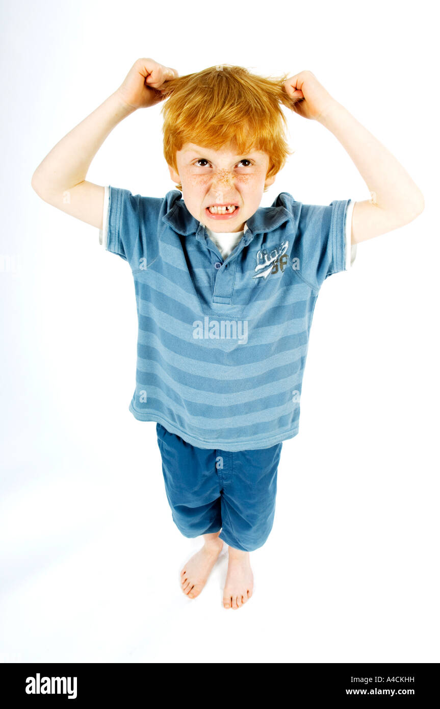Giovane ragazzo in blu su bianco goccia per tagliare tirando i suoi capelli in frustrazione mentre cercando in rabbia Foto Stock
