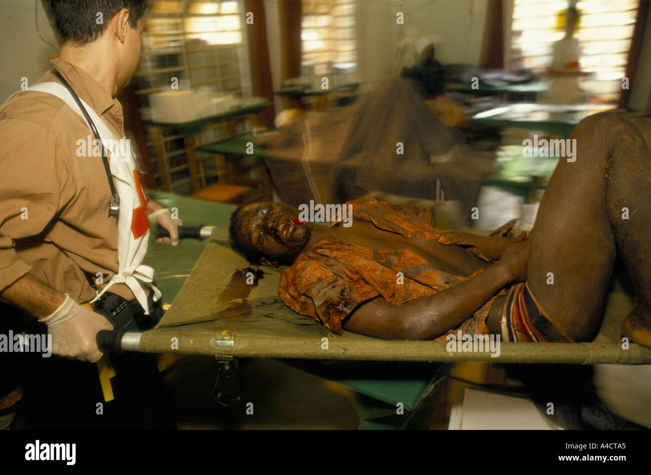 "Ruandese GUERRA CIVILE', tutsi tritato uomo attraverso la testa dai colpi di machete è portato su una barella DA UN MEMBRO DELLA CROCE ROSSA internazionale del team chirurgico. Aprile 1994 Foto Stock