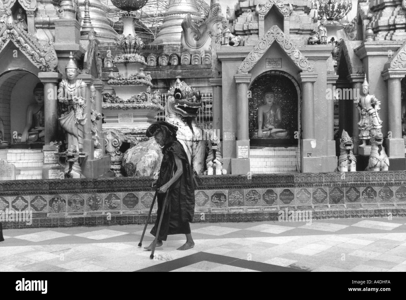 Un monaco buddista sulle stampelle è a piedi nella parte anteriore della Shwedagon Paya tempio, Yangon, Rangoon, MYANMAR Birmania Foto Stock