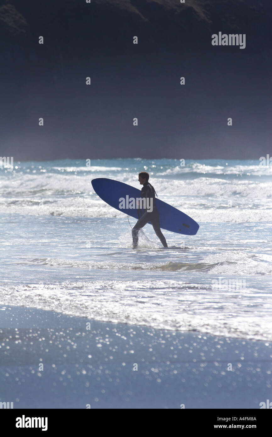 Surfer tornando dal mare contro la luce solare Perranporth Cornovaglia Foto Stock