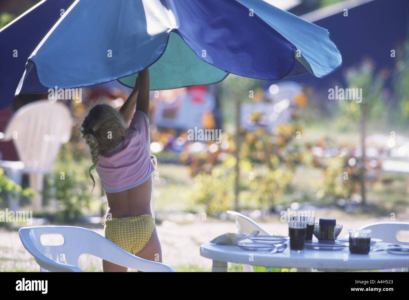 Una giovane ragazza regola l'ombrellone presso il tavolo per la colazione su un camping vacanze in Bretagna, Francia. Foto Stock