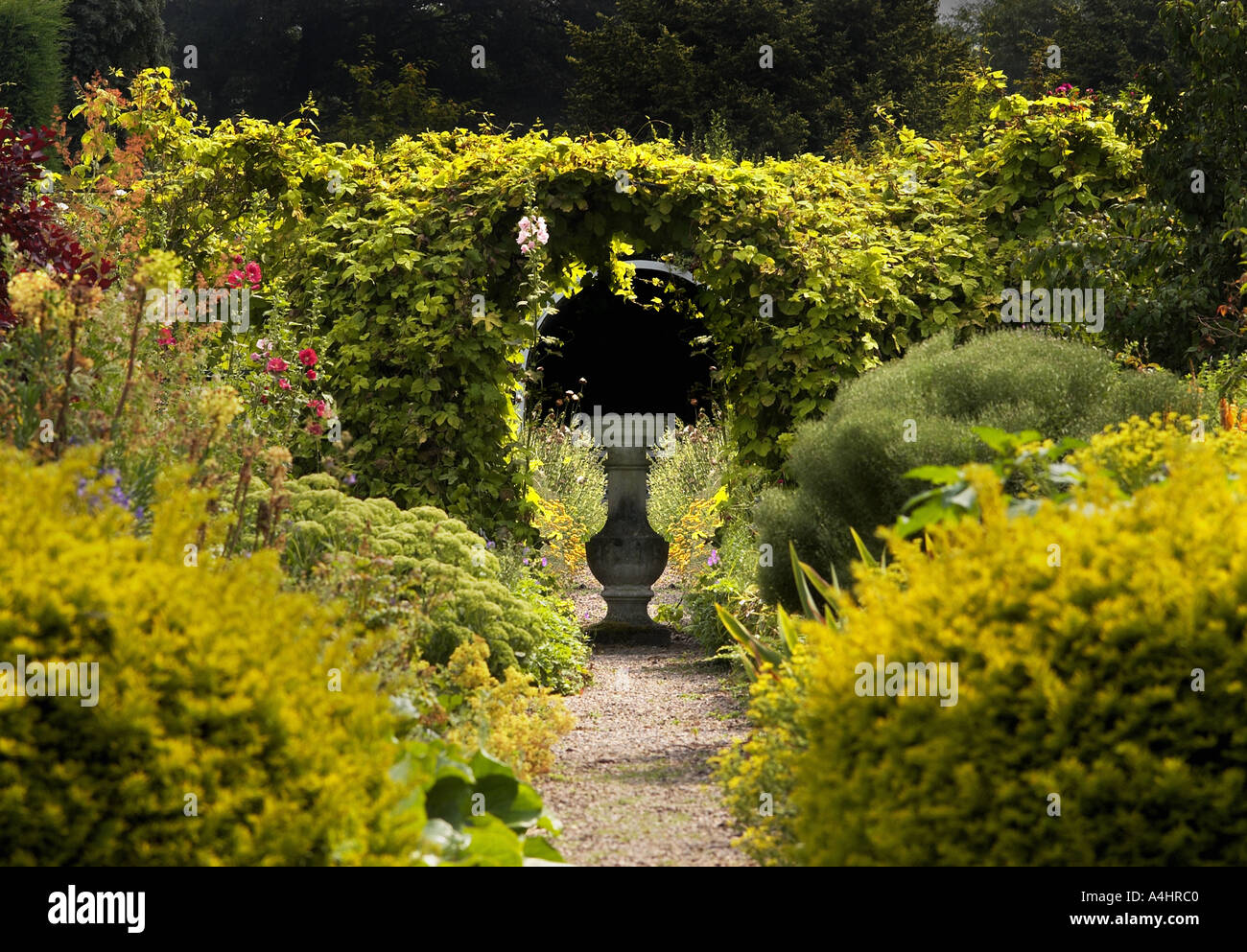 Percorso attraverso il naturale paese inglese giardino che conduce a archway in hedge con pietra centrale Ornamento da giardino Foto Stock