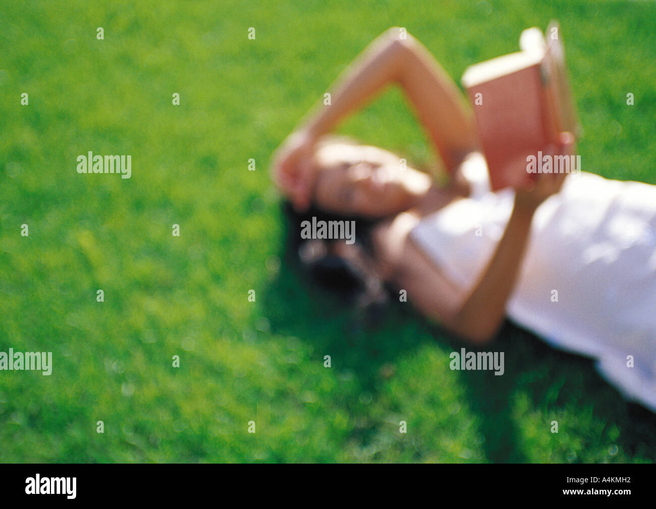 Donna sdraiata su erba, lettura, sfocato Foto Stock