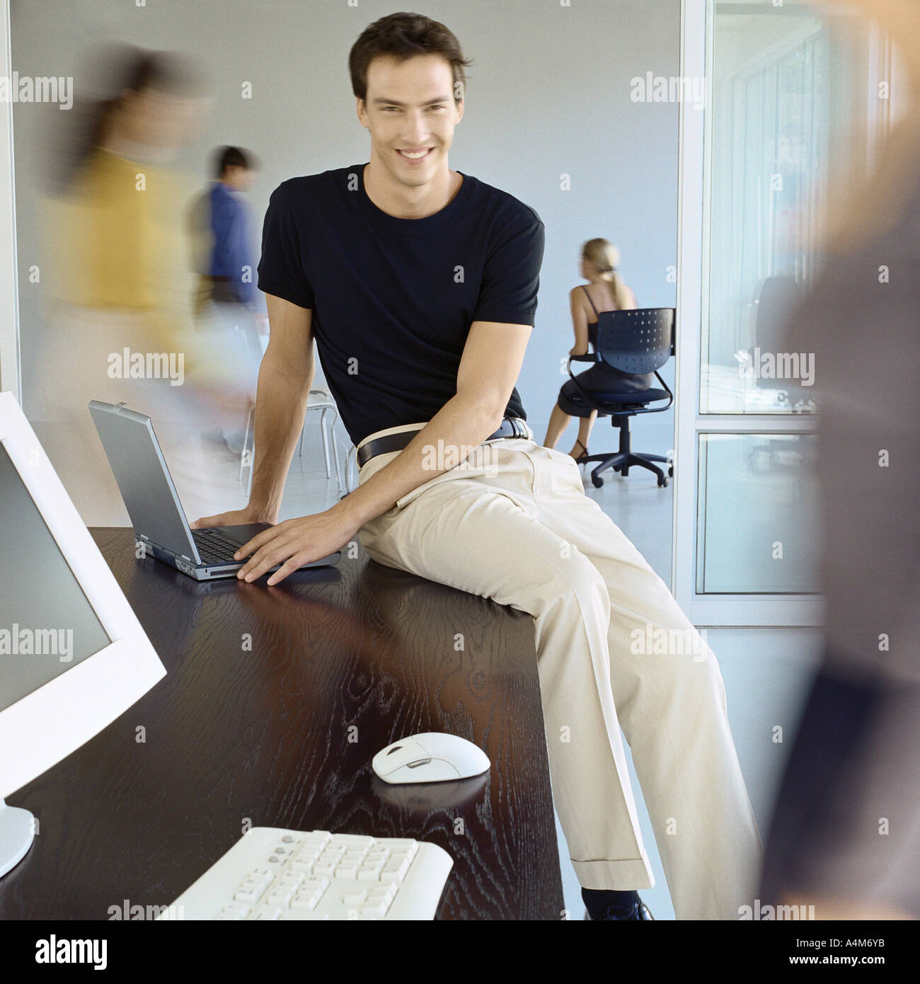 Uomo seduto sul bordo della scrivania in ufficio occupato Foto Stock