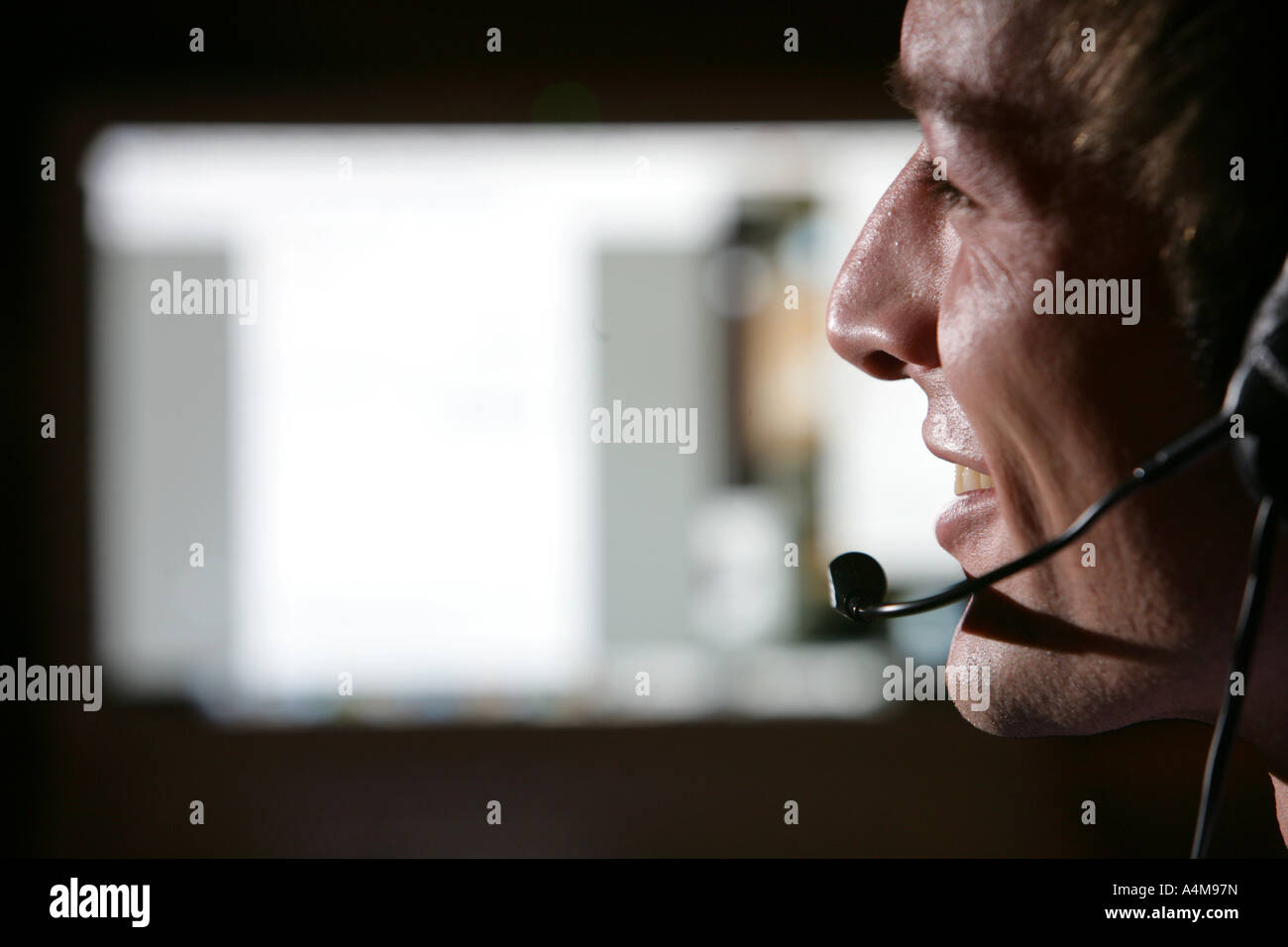 Persona di sesso maschile si sta parlando al telefono e Internet, Voice over IP, usando un auricolare con microfono, nella parte anteriore del monitor di un computer. Foto Stock