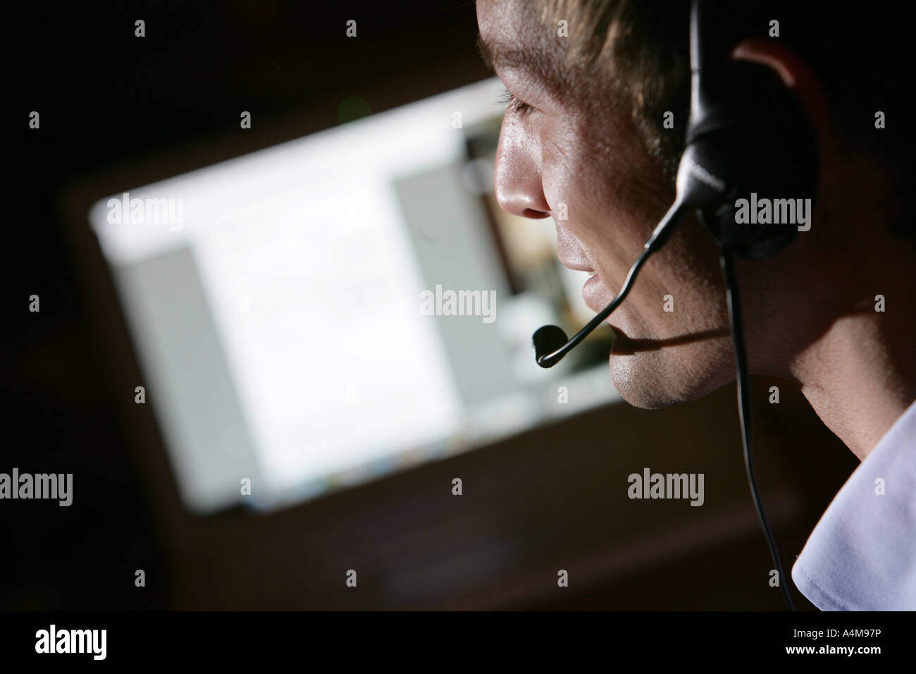 Persona di sesso maschile si sta parlando al telefono e Internet, Voice over IP, usando un auricolare con microfono, nella parte anteriore del monitor di un computer. Foto Stock