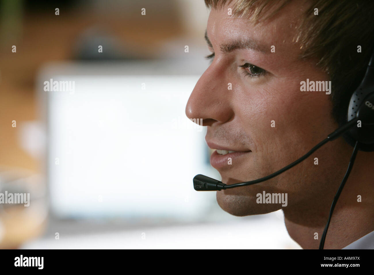 Persona di sesso maschile si sta parlando al telefono e Internet, Voice over IP, usando un auricolare con microfono, nella parte anteriore del monitor di un computer. Foto Stock