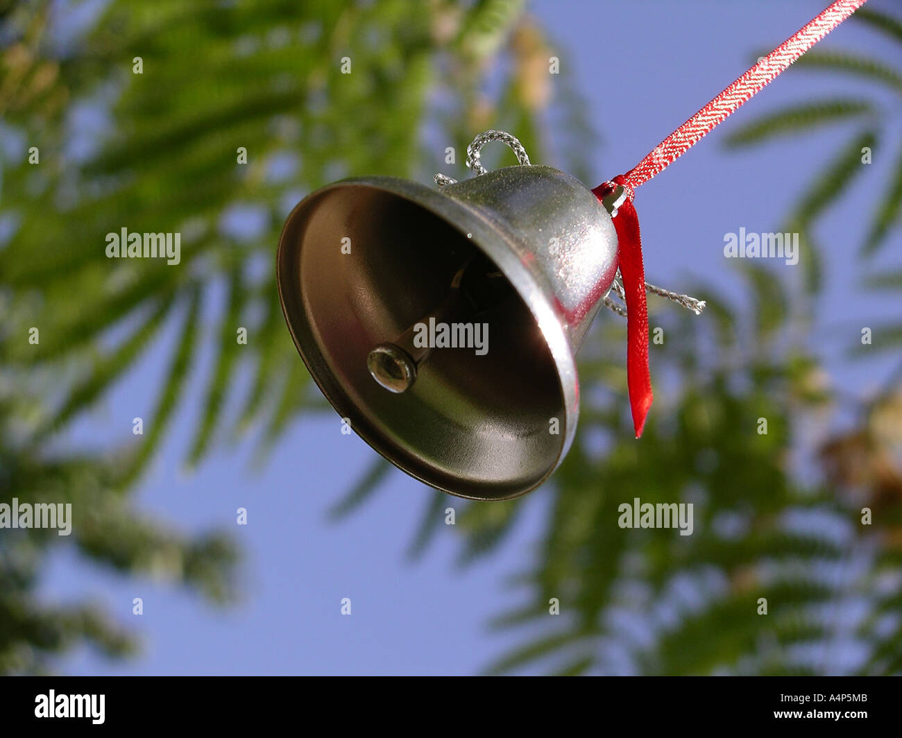 Campana di argento è appeso a un filo rosso da un albero con il blu del cielo Foto Stock