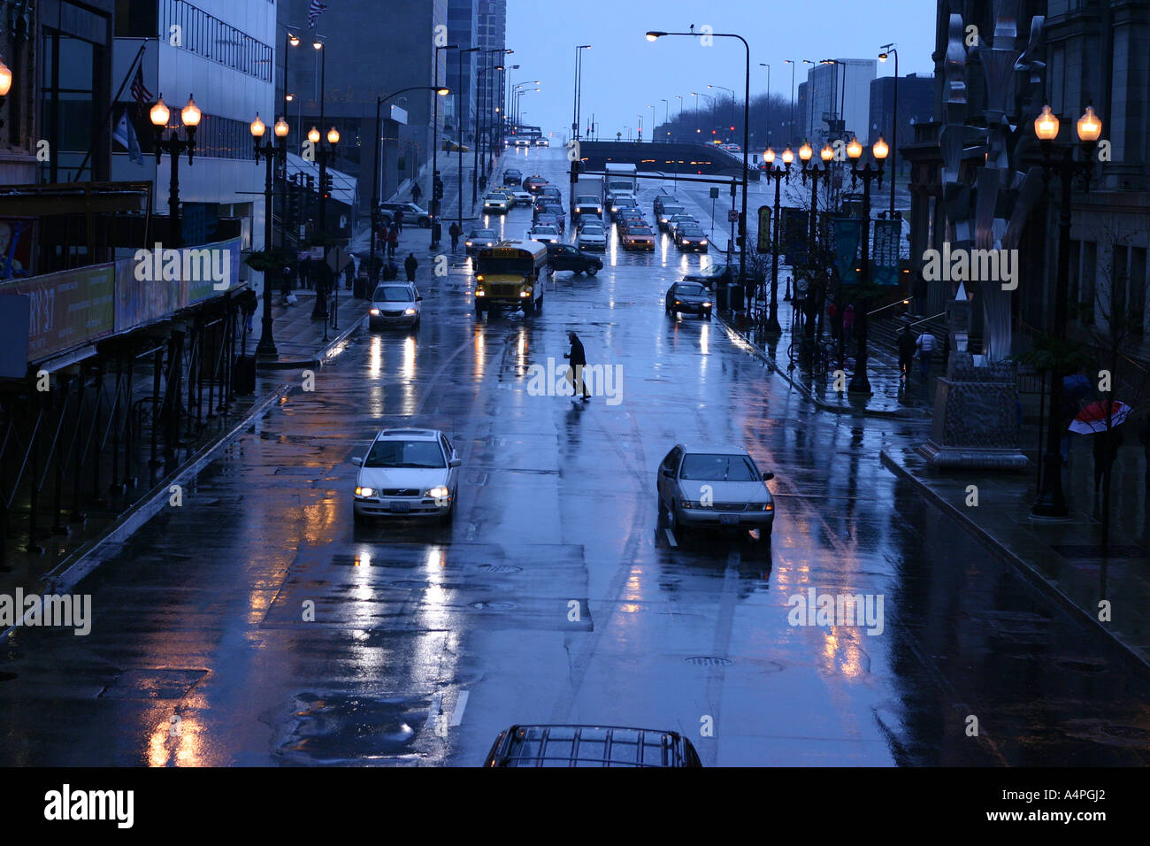 L'uomo attraversando Cars driving attraverso un incrocio occupato in una piovosa e bagnato notte su Randolph Street , downtown Chicago, Stati Uniti d'America Foto Stock