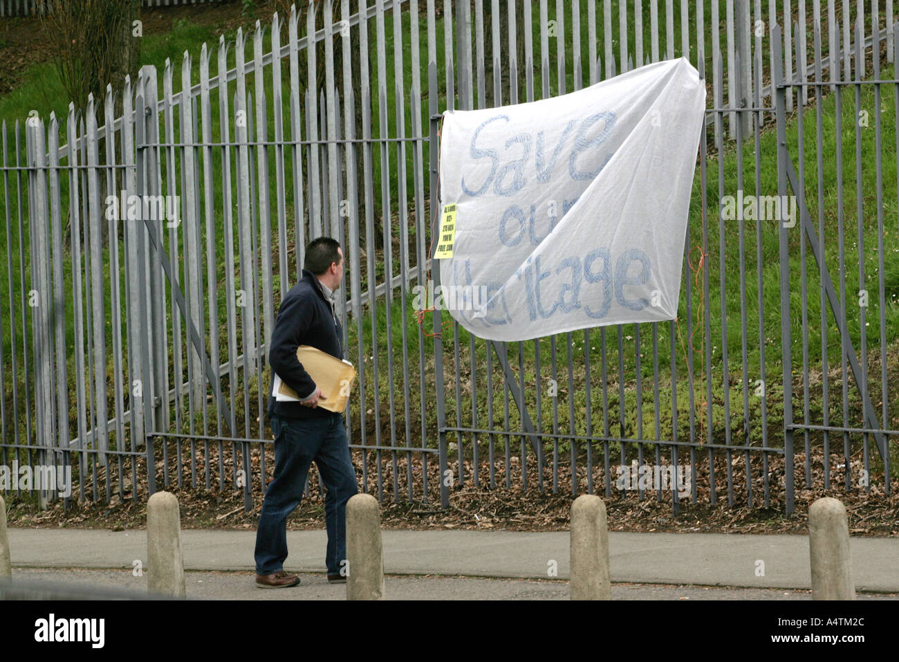 Un uomo cammina davanti a un dipinto a mano segno con lo slogan di salvare il nostro patrimonio al di fuori del Rover fabbrica di automobili a Longbridge Birmingham Foto Stock