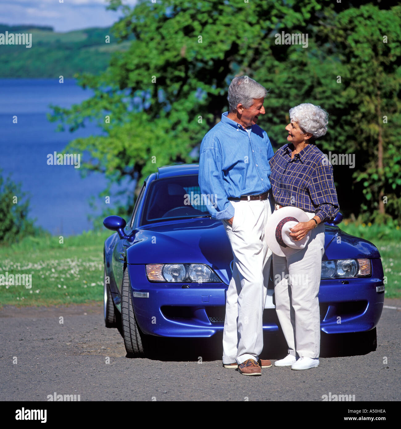 Coppia matura in piedi accanto a parlare di una vettura sportiva a Loch Lomond Scozia Scotland Foto Stock