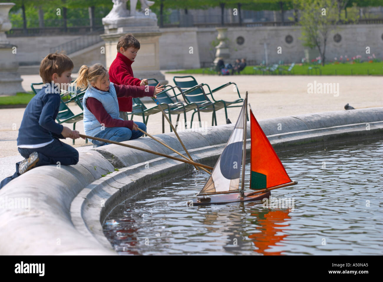 Bambini che giocano con un modello di barca su un lago in giardini Tuileries Parigi Francia Foto Stock