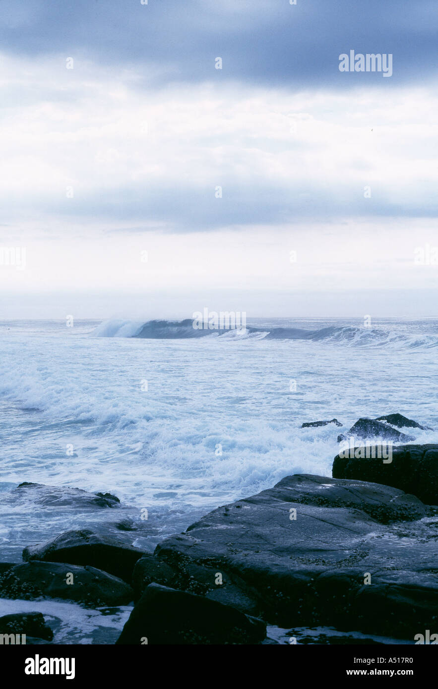 Onde che si infrangono con moody sky, e reef in primo piano Foto Stock