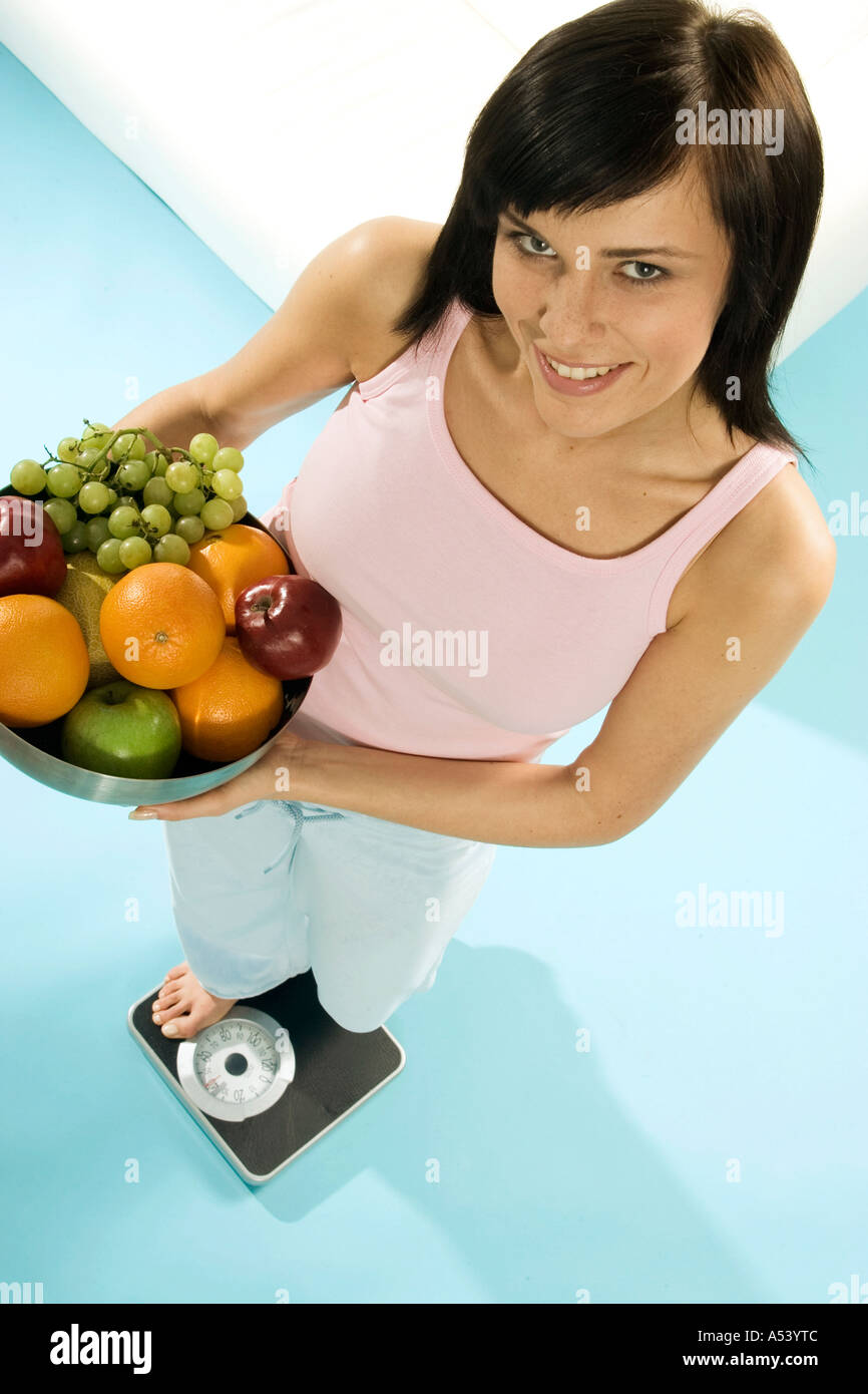 Giovane donna in piedi su una bilancia con una cesta di frutta Foto Stock