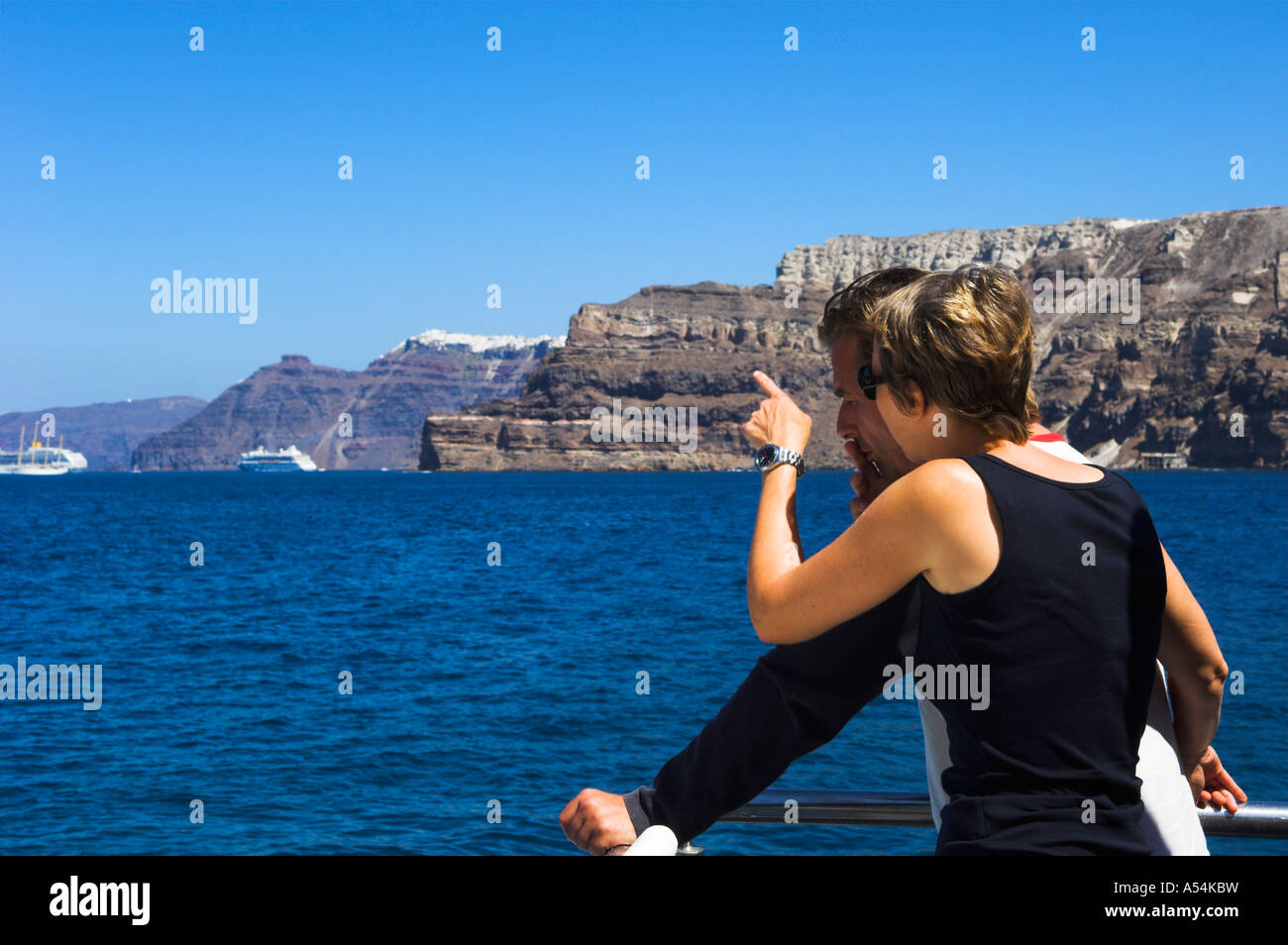 Donna con partner maschio rivolta verso le rupi scoscese e la città di Thira isola di Santorini dalla barca in mare Foto Stock