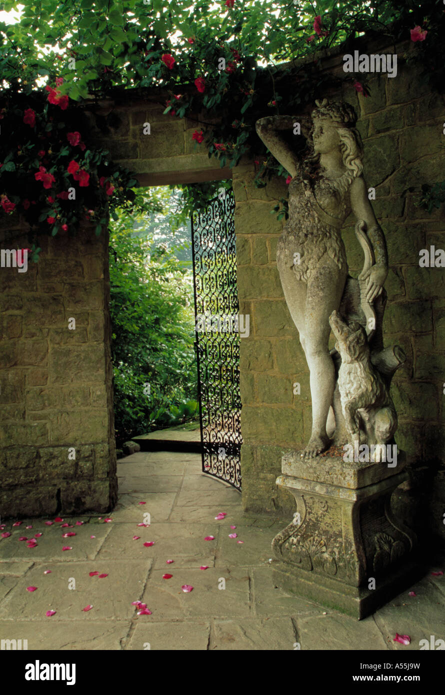 Statua classica su zoccolo in pietra accanto a Apri porta di metallo nel muro e vista del giardino a Pashley Manor nel Sussex Foto Stock