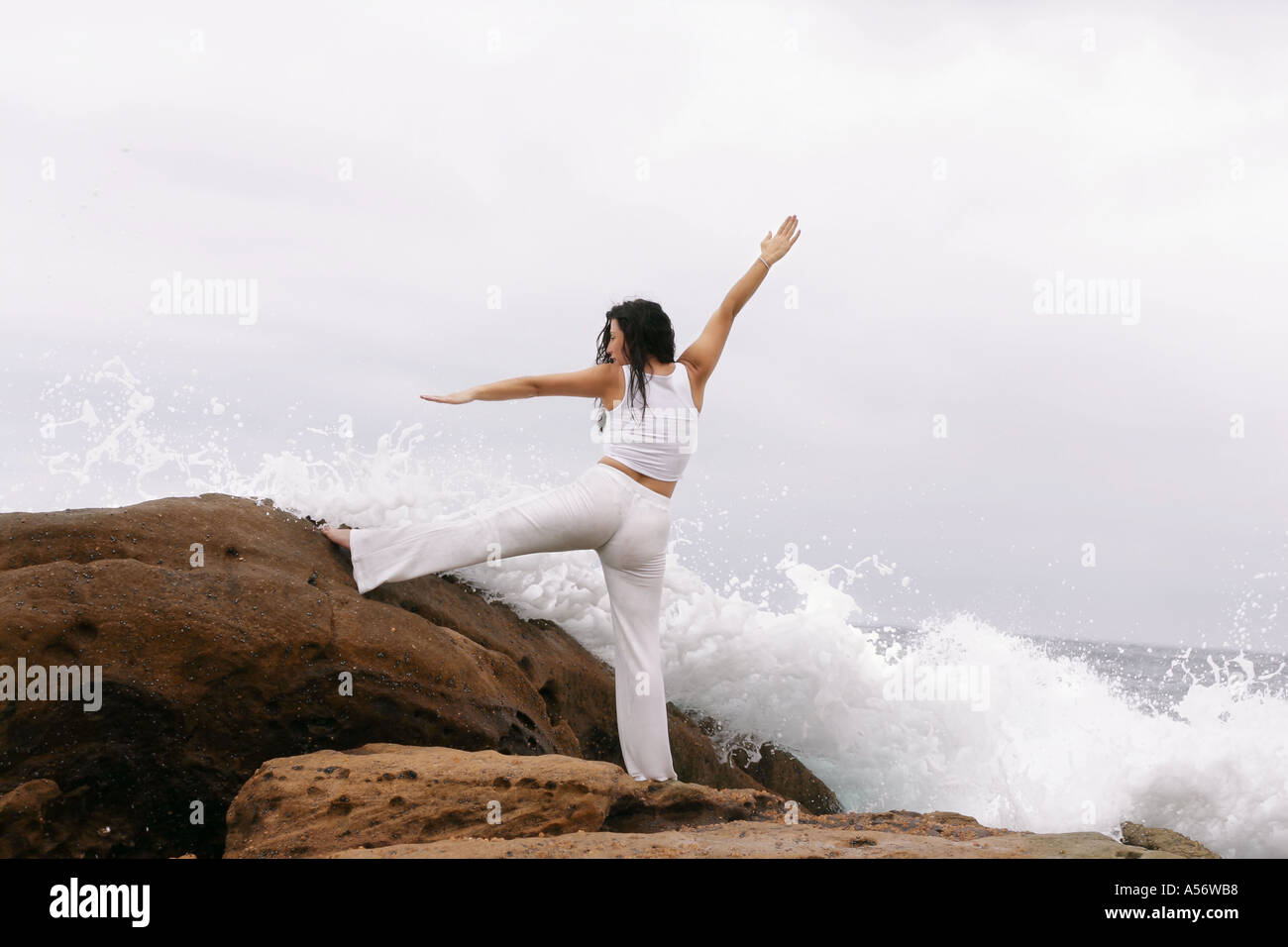 Donna attiva si estende su wave spazzata di rocce Foto Stock