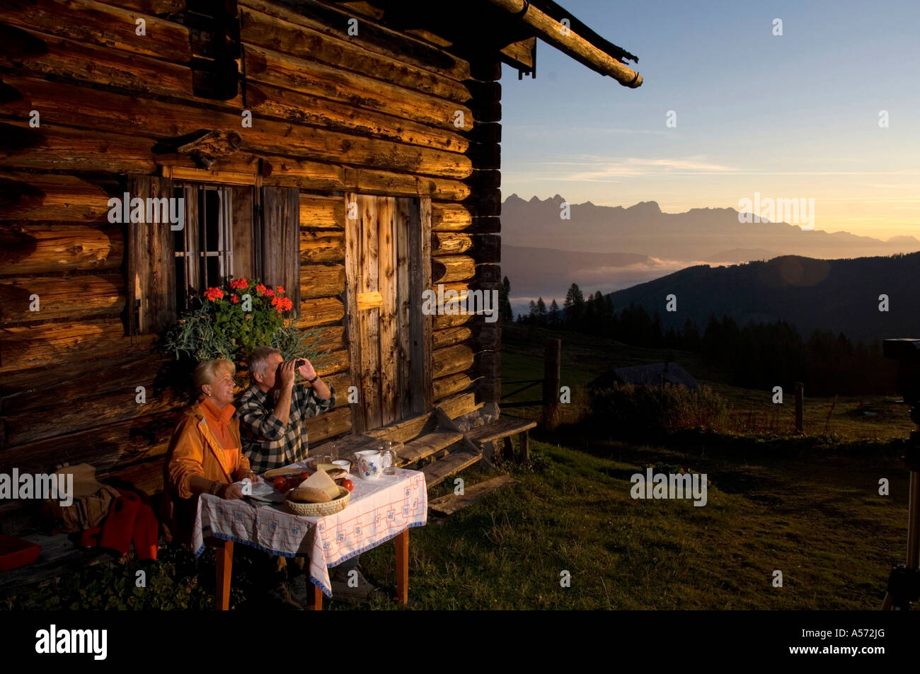 Coppia matura seduti davanti al rifugio alpino, guardando il tramonto Foto Stock