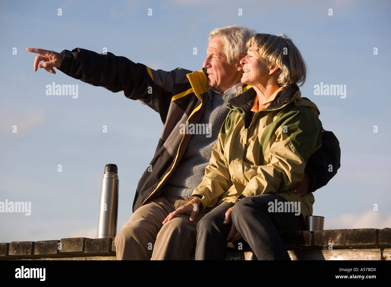 Coppia senior seduta sul molo, un uomo indica Foto Stock