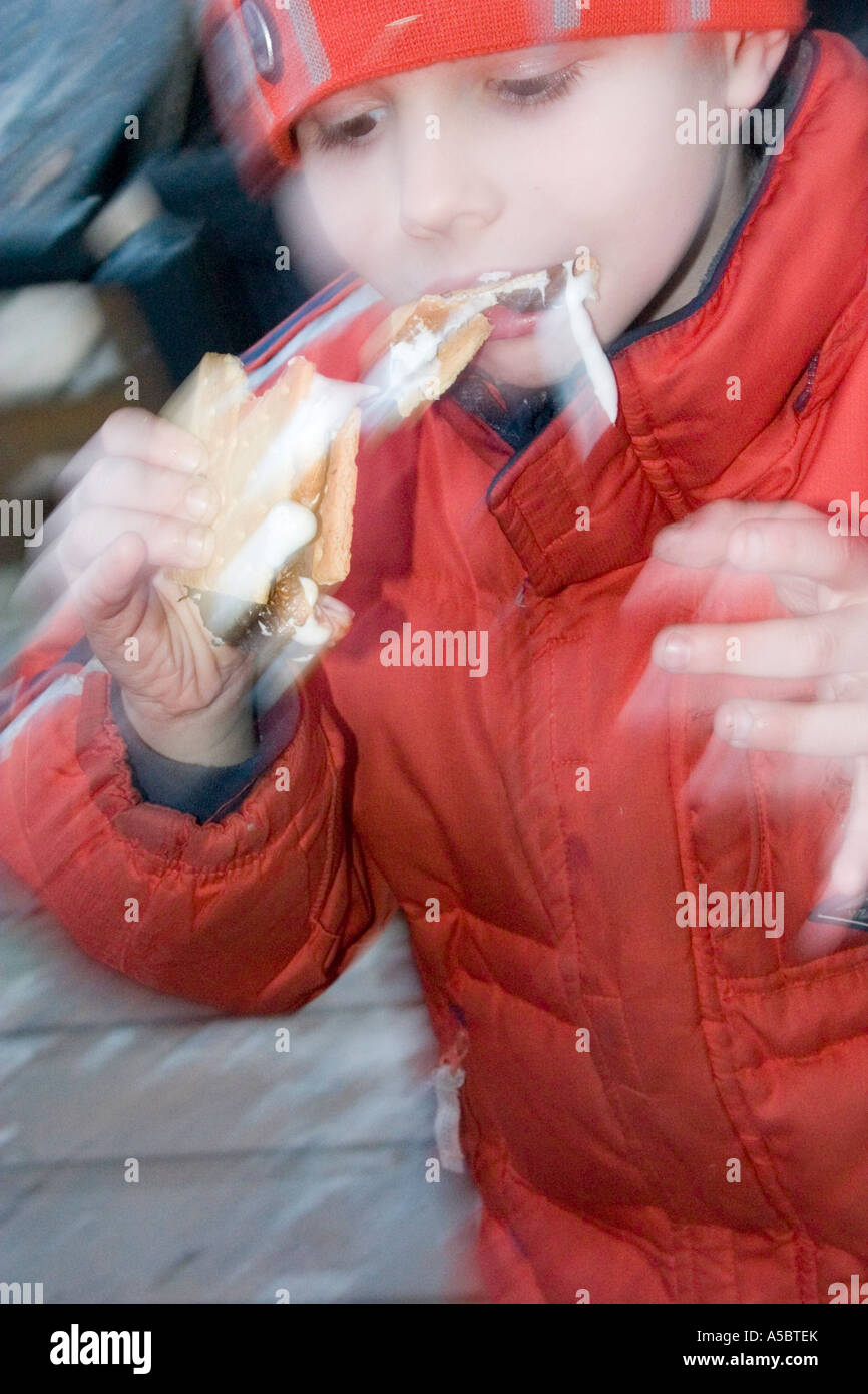 Blur boy 6 anni di mangiare un smore da squishing riscaldata marshmallow e cioccolato tra graham cracker. Clitherall Minnesota USA Foto Stock