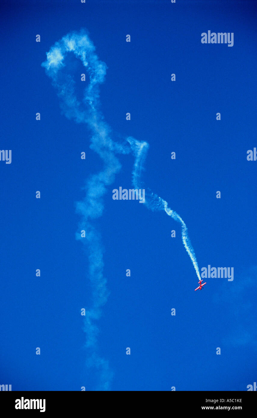 Piccolo aereo rosso di coda di fumo bianco di eseguire acrobazie aeree contro un profondo cielo blu Foto Stock