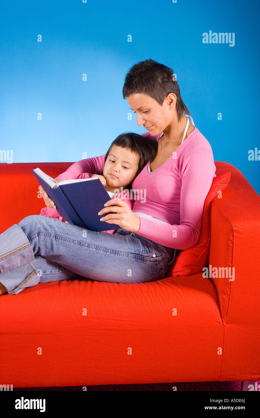 La donna e la sua dauther seduto sul divano rosso e la lettura del libro Foto Stock