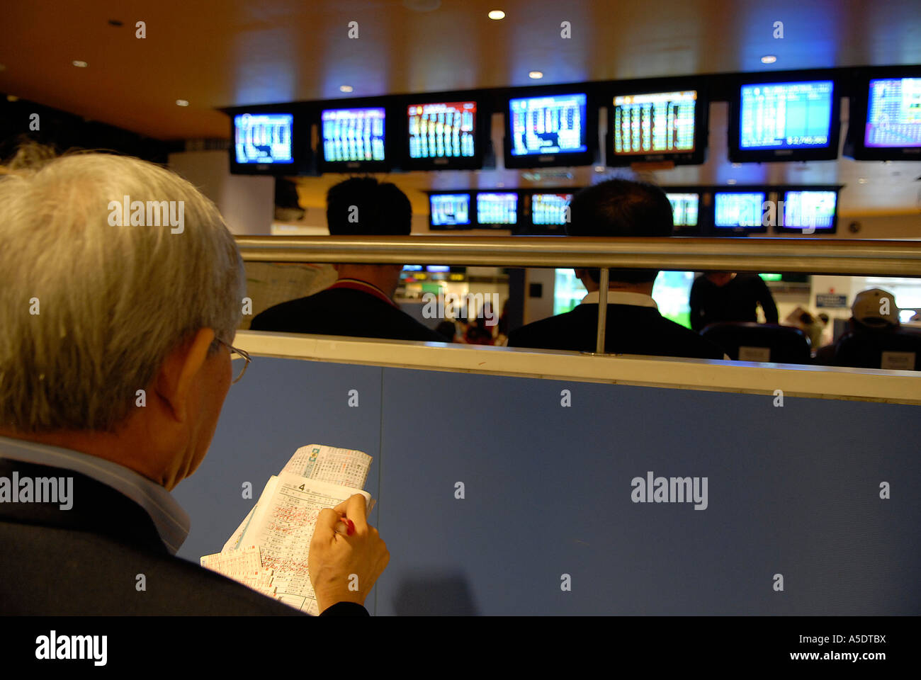 I puntatori guardano gli schermi digitali che mostrano i risultati delle gare in Sala pubblica di scommesse dell'Ippodromo di Sha Tin a Hong Kong Cina Foto Stock