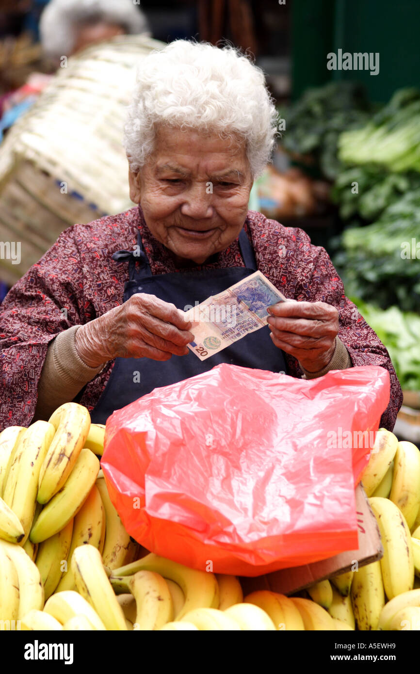 Di Hong Kong, Kowloon, vecchia donna la vendita delle banane nel mercato controlla un bill, Cina Foto Stock