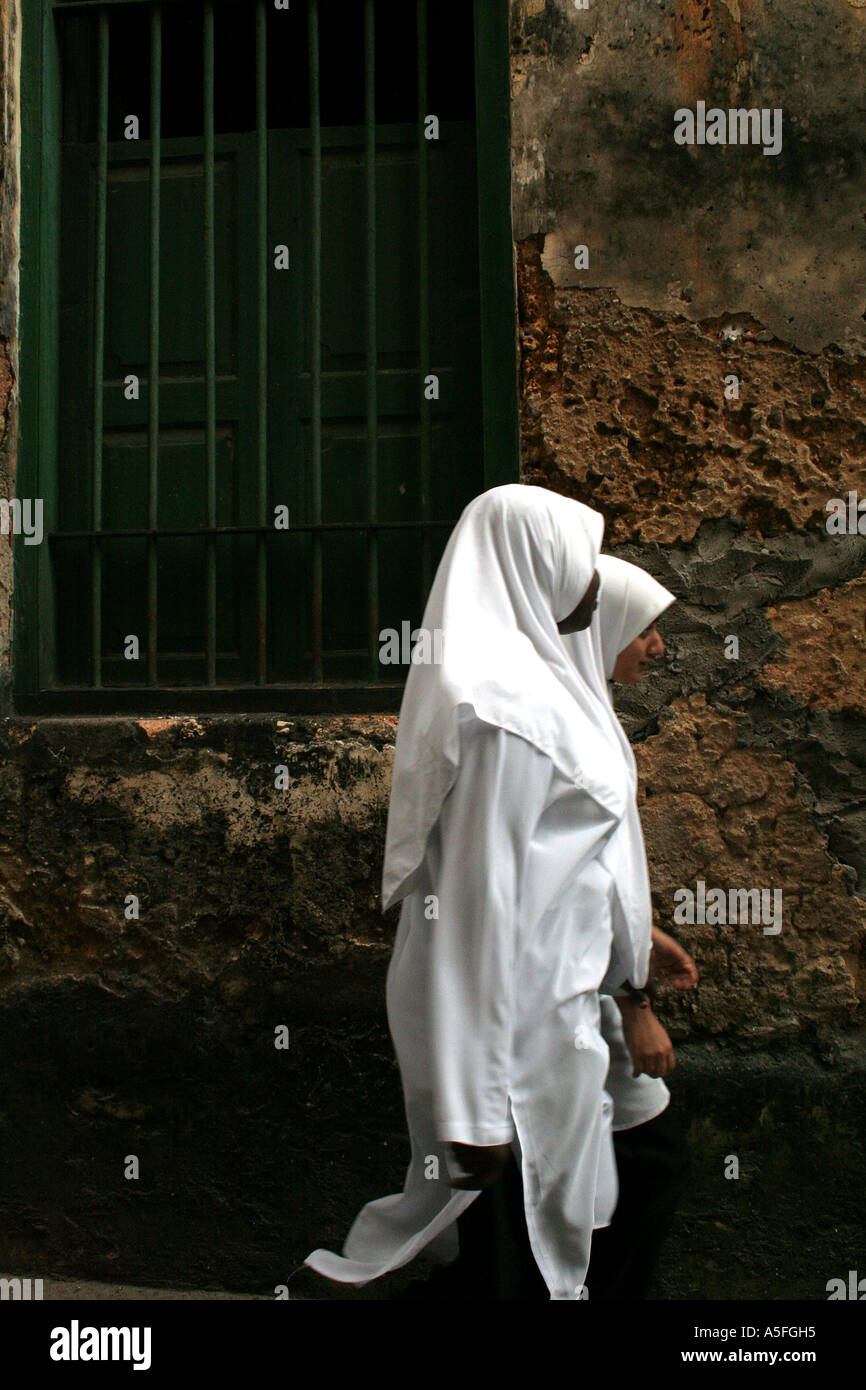 Due ragazze a piedi attraverso le strette strade di Stonetown, Zanzibar, Tanzania Foto Stock