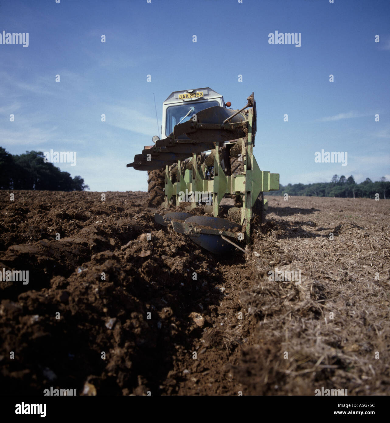 Retro dell'aratro dal basso angolo di visione del trattore arare il terreno e essiccato prati con cielo blu Foto Stock
