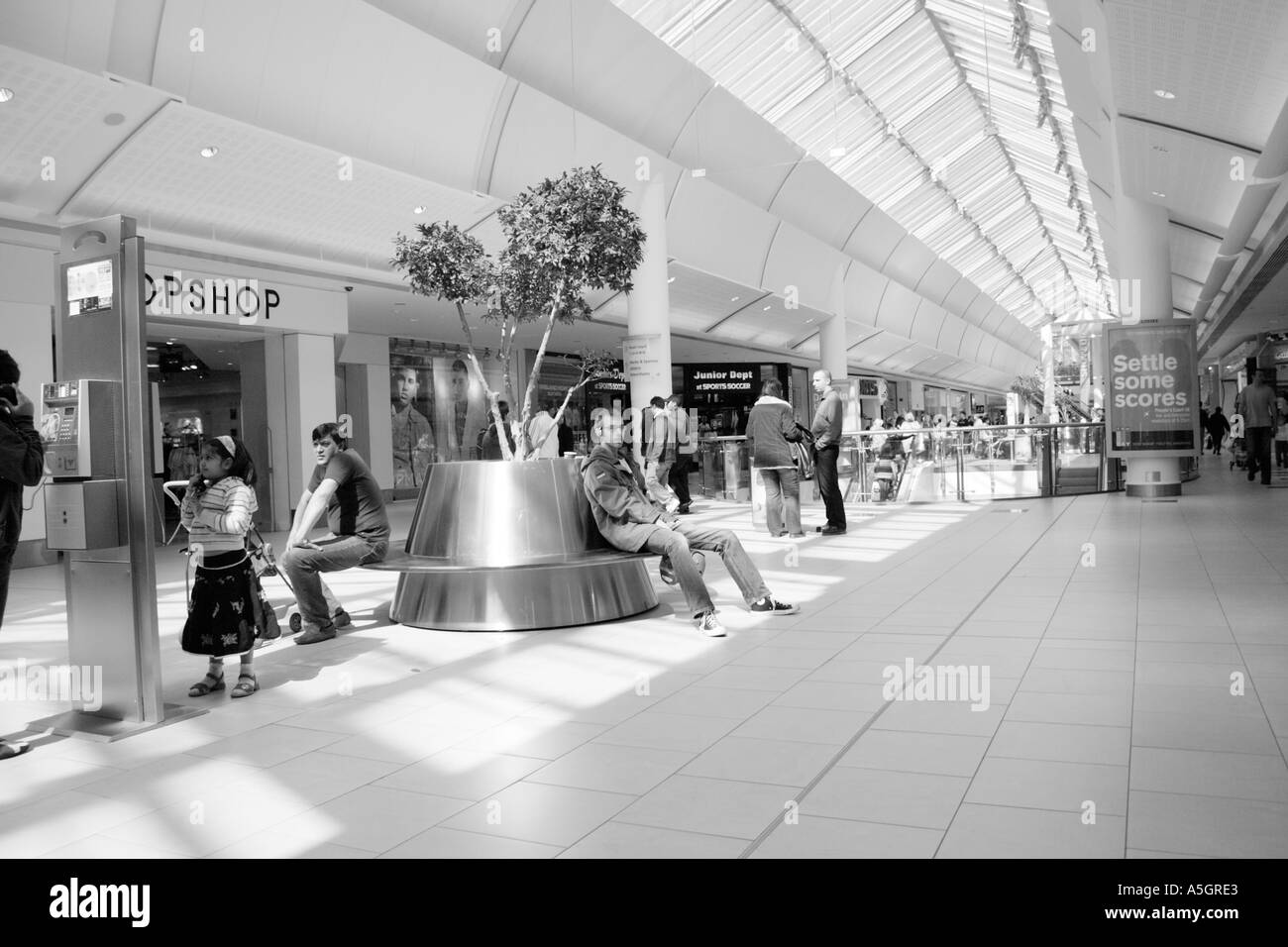Immagine in bianco e nero fuori un affollato centro commerciale, partite fuori la gente a piedi circa e sedersi in appoggio sui banchi Foto Stock