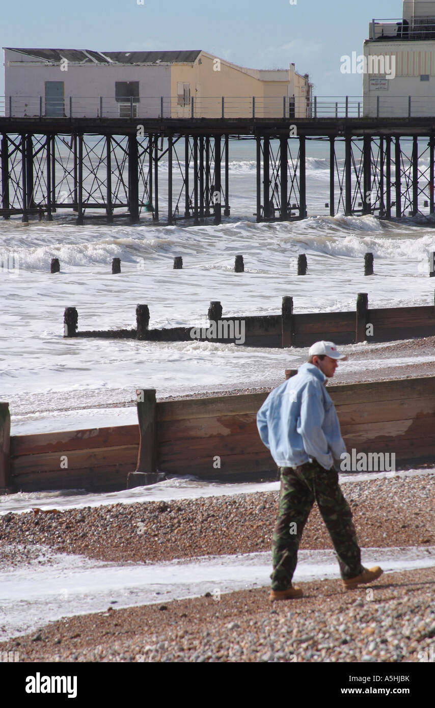 Uomo che cammina su ciottoli vicino a Bognor Regis Pier a marea alta. Foto Stock