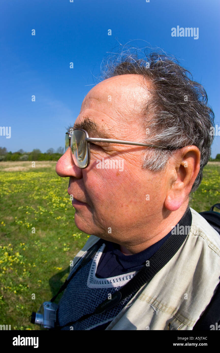 L'uomo con la fotocamera in piedi nel campo di erba con cielo blu e cowslips in background Foto Stock