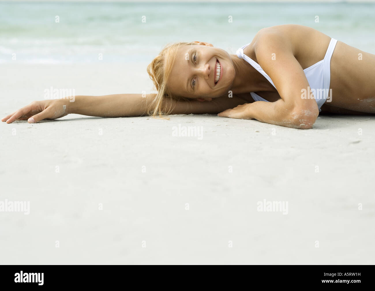 Donna sdraiata sulla spiaggia, sorridente in telecamera Foto Stock