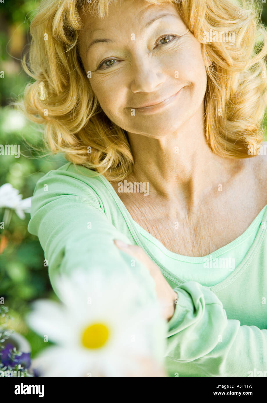 Senior donna tenendo fuori fiore, ritratto Foto Stock