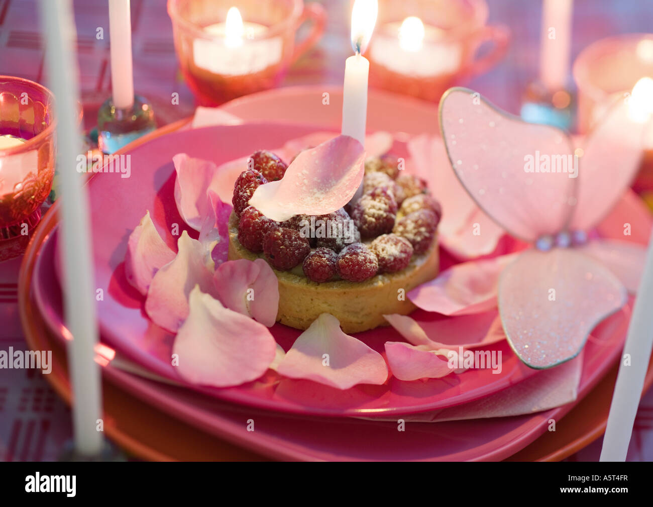 Lampone pasticceria su lastra decorata con petali di rosa e candele Foto Stock