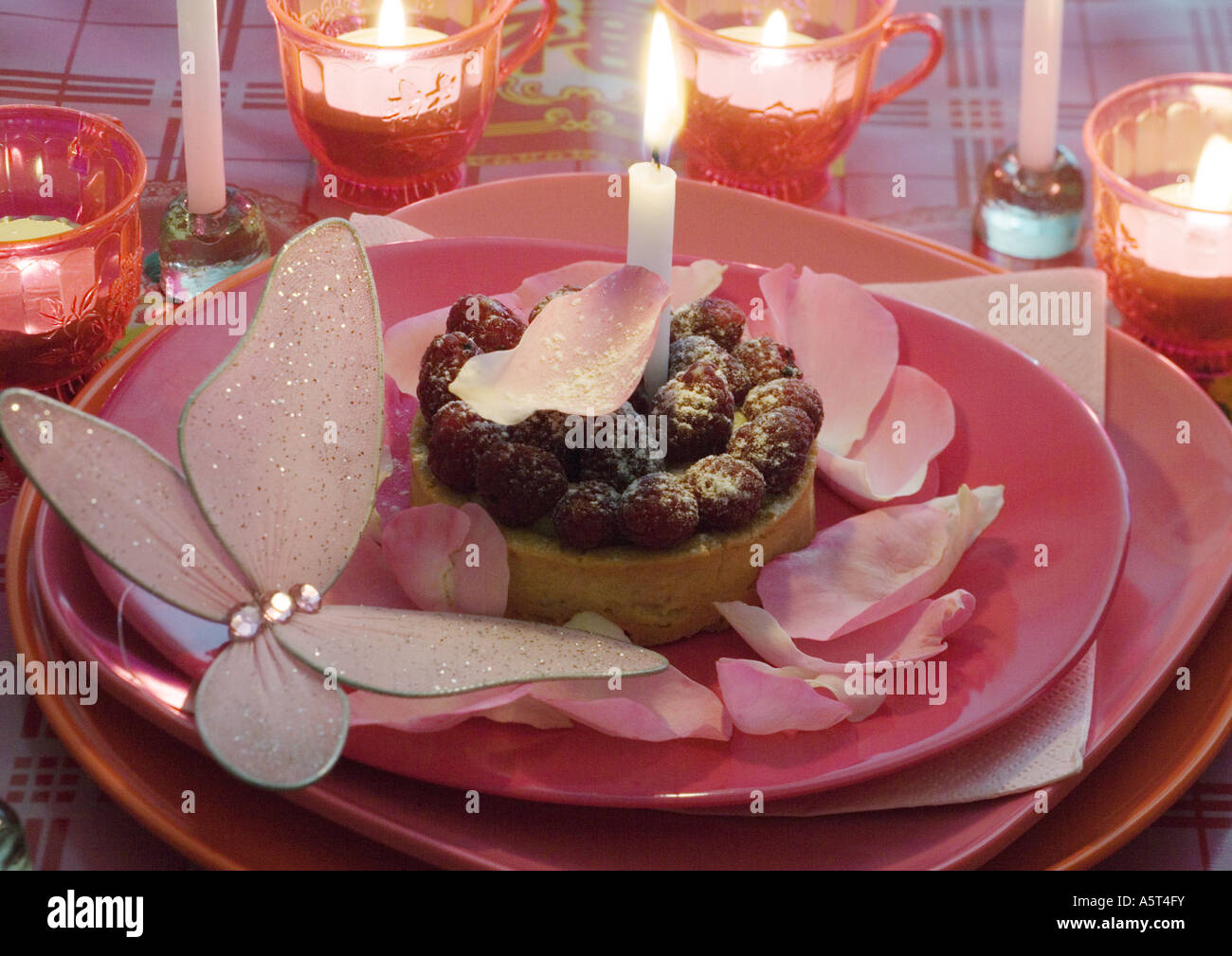 Lampone pasticceria su lastra decorata con petali di rosa e candele Foto Stock
