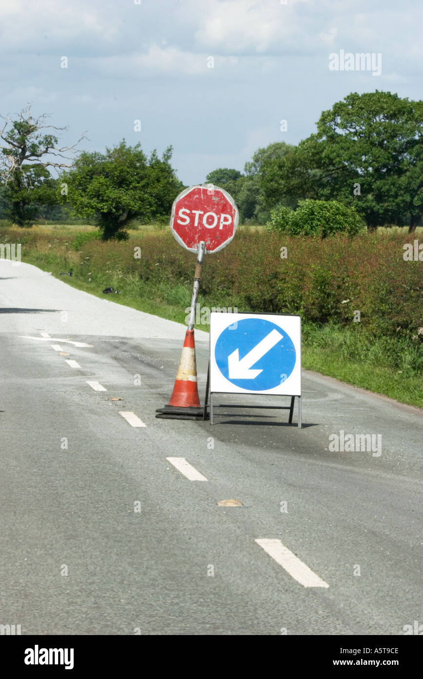 Il segnale di arresto e nella direzione della freccia segno a lavori stradali su un Inglese nazione road blu punti freccia sinistra Foto Stock