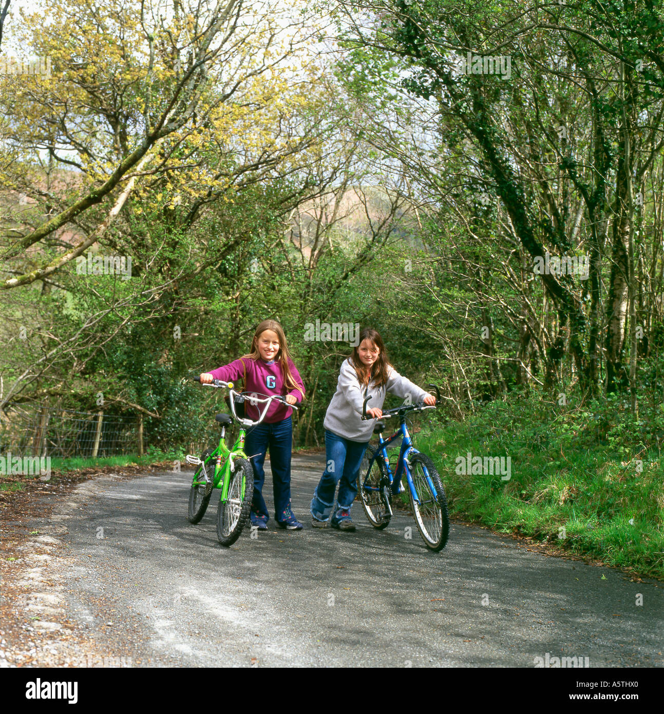 Amici ragazza ragazze spingendo bike bicicletta fino alla cima di una collina su un vicolo del paese in primavera in Galles Carmarthenshire UK KATHY DEWITT Foto Stock