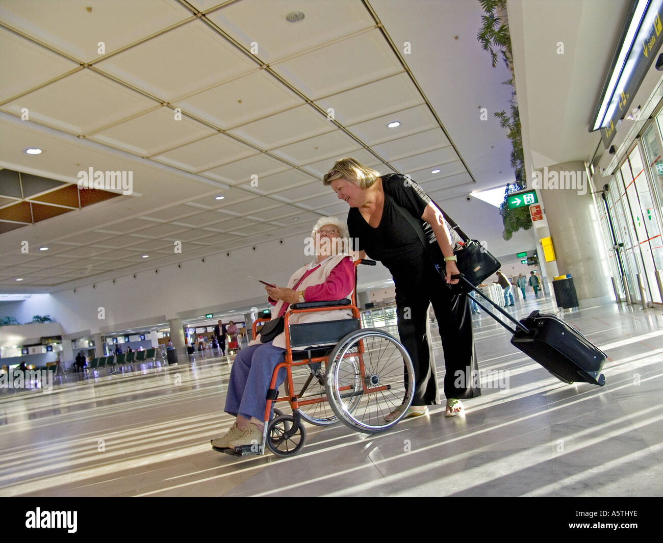 Donna anziana in carrozzina con accompagnatore femmina sul compagno aeroporto concourse Preparazione al Viaggio Foto Stock