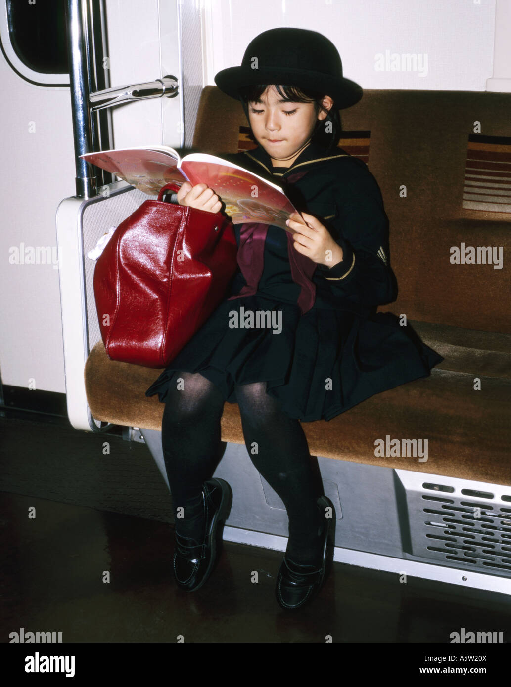 Ragazza giovane,perfettamente vestito nella sua uniforme scolastica,legge da un libro sul treno della metropolitana,Tokyo, Giappone. Foto Stock