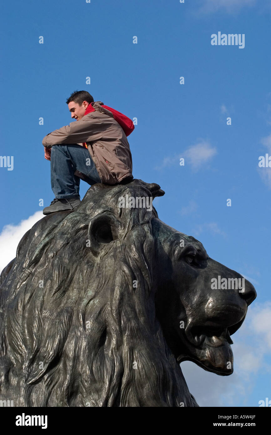 Turismo maschile seduto su Landseer Lion statua. Trafalgar Square a Londra, Inghilterra Foto Stock