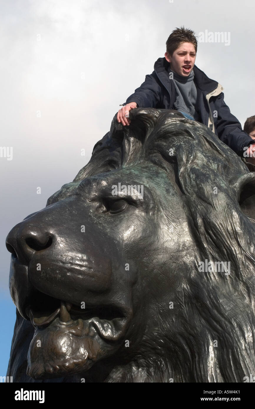 Turismo maschile seduto su Landseer Lion statua. Trafalgar Square a Londra, Inghilterra Foto Stock