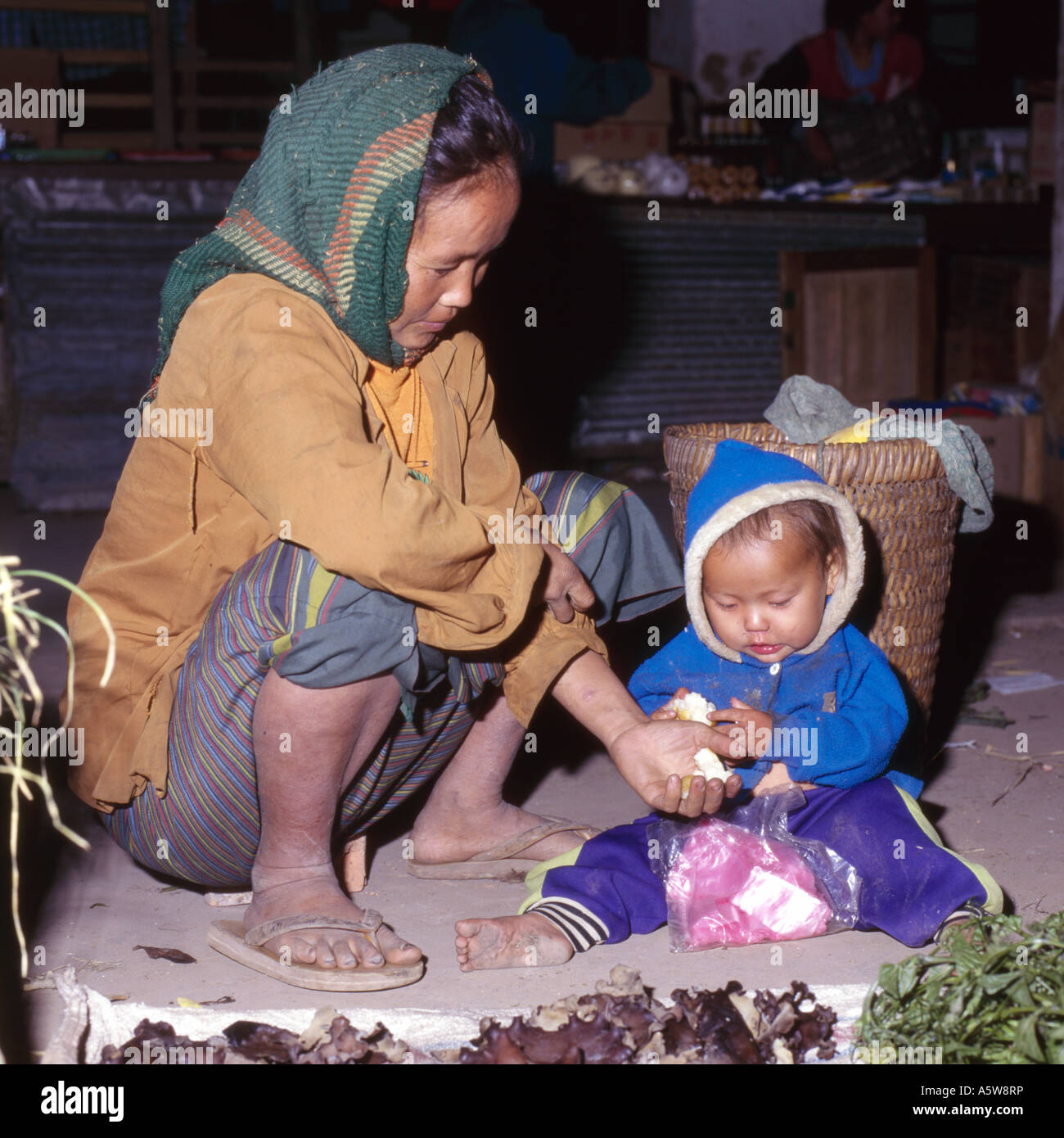 Locali di madre e bambino,poveramente vestito,la vendita di alcune verdure da una piccola area sul terreno,Muang cantare mercato,Nord del Laos. Foto Stock