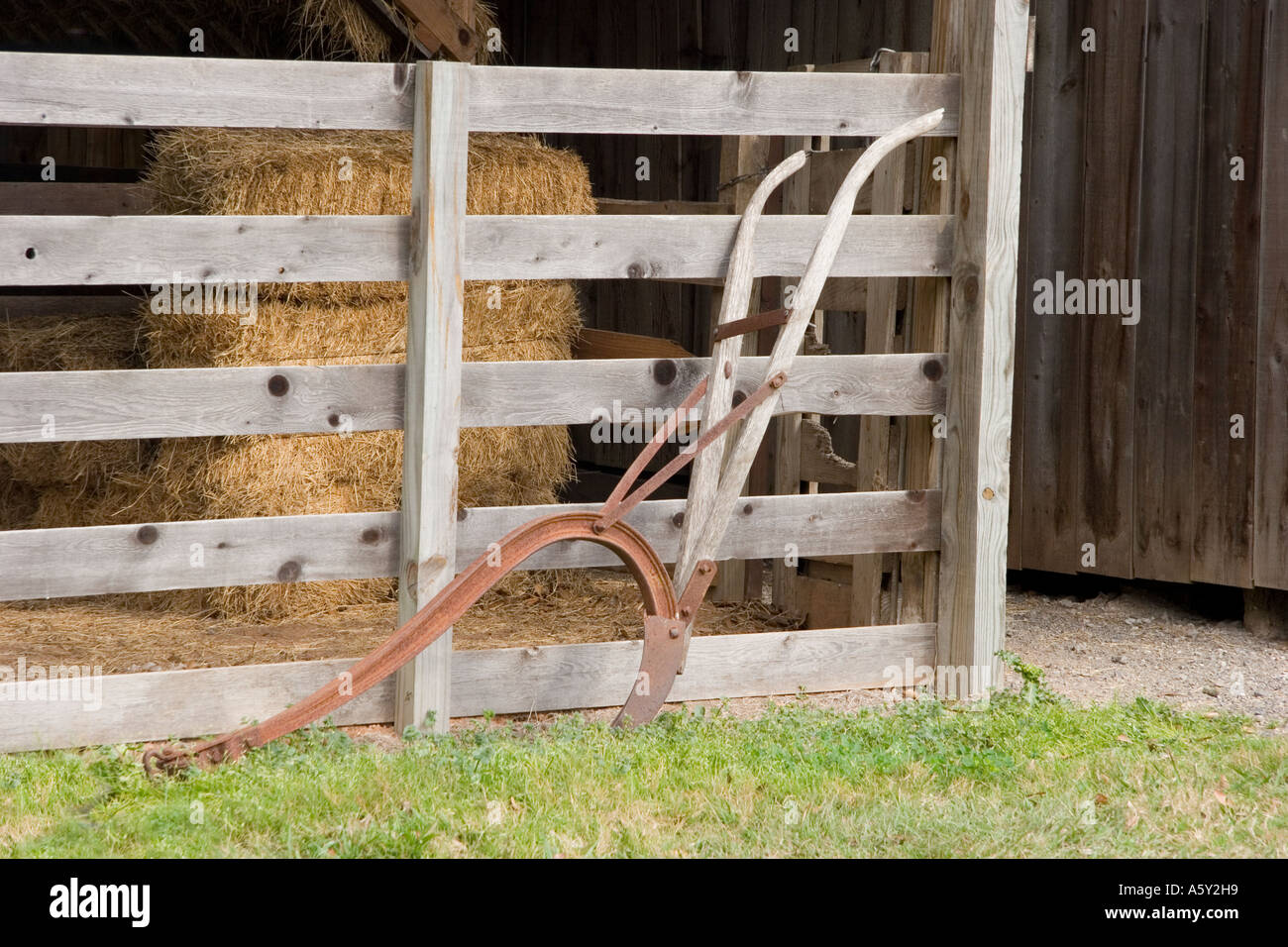 Antico aratro a mano si appoggia sulle stecche di recinzione di legno, la  balla di fieno, vecchio muro del granaio Foto stock - Alamy