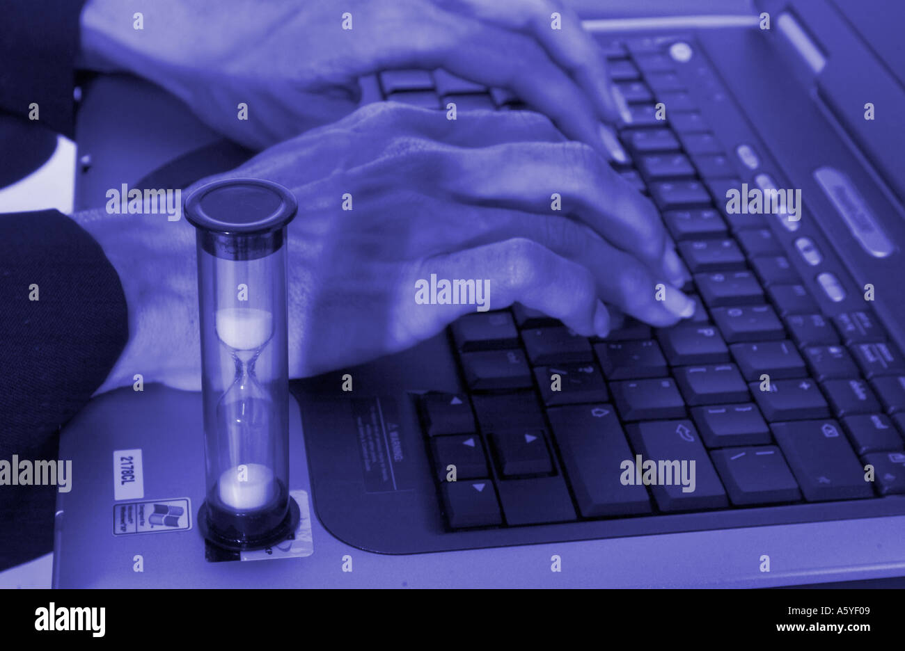 Donna che scrive su un laptop con una clessidra accanto, simboleggiando la gestione del tempo e la produttività, USA. Foto Stock