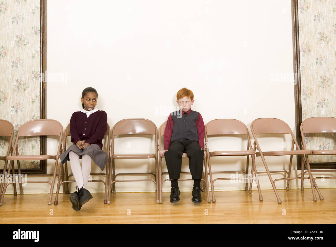 Ragazzo e una ragazza seduta in sedie contro la parete Foto Stock