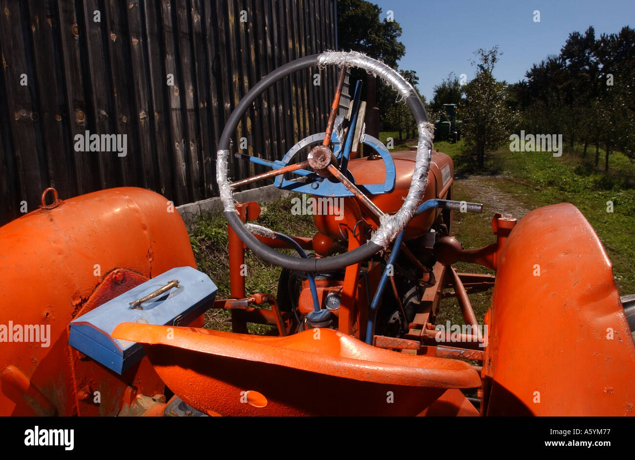 Un luminoso rosso arancione del trattore su una fattoria accanto ad un fienile apple Orchard Foto Stock